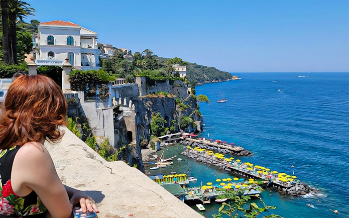 Woman overlooking Amalfi Coast with colorful beach umbrellas and cliffs.