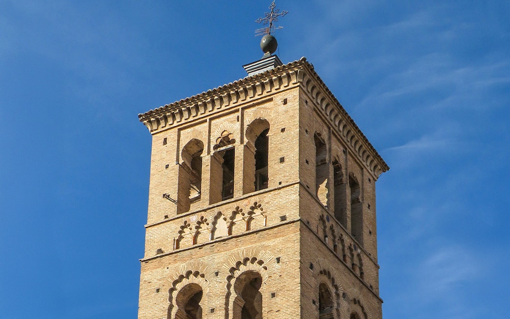 Bell tower of Church of St. Tomé in Toledo against blue sky.