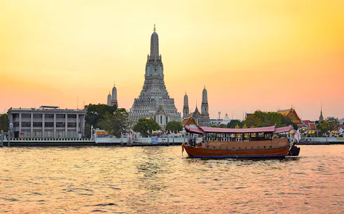 Traditional boat on Chao Phraya River with Wat Arun temple at sunset, Bangkok.