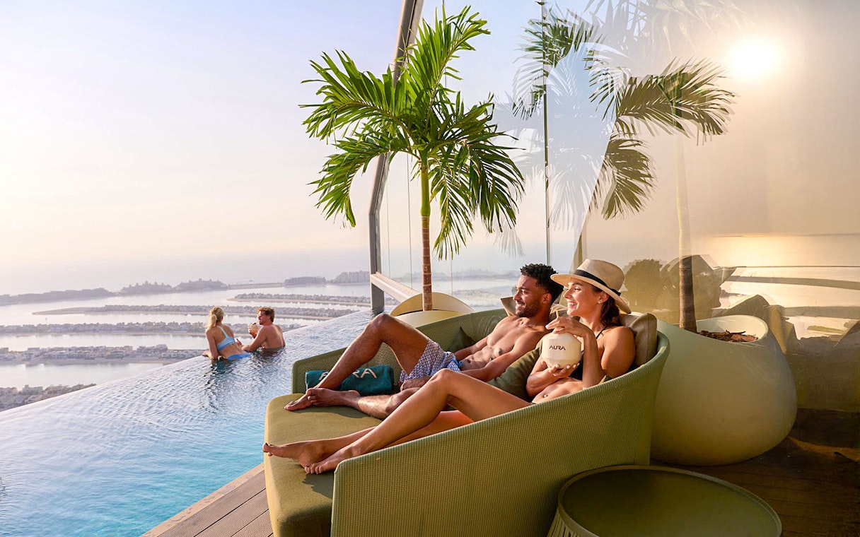 Couples relaxing by the pool at AURA Sky Pool with a view of Palm Jumeirah.