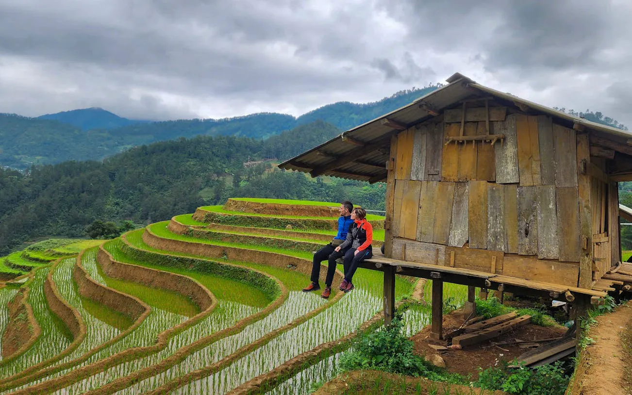 Couple sitting by wooden hut overlooking terraced rice fields in Mu Cang Chai, Vietnam.