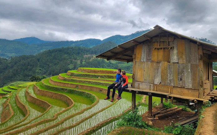Couple sitting by wooden hut overlooking terraced rice fields in Mu Cang Chai, Vietnam.