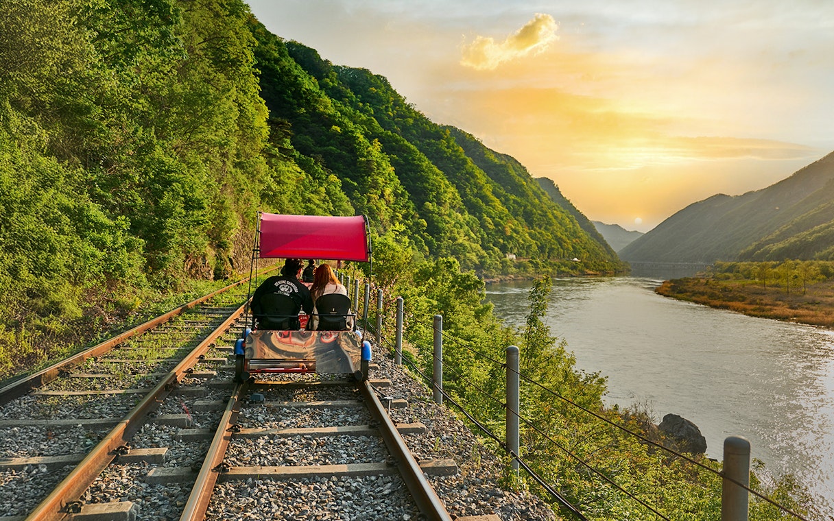 Couple on Gangchon rail bike along river at sunset, Nami Island.