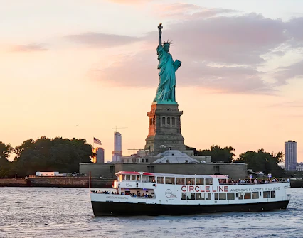 Statue of Liberty at sunset with Circle Line cruise boat in New York Harbor.