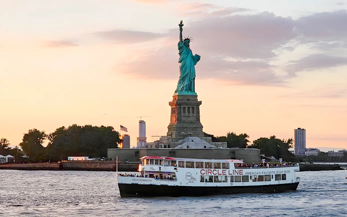 Statue of Liberty at sunset with Circle Line cruise boat in New York Harbor.