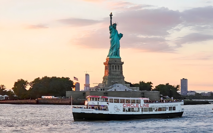 Statue of Liberty at sunset with Circle Line cruise boat in New York Harbor.