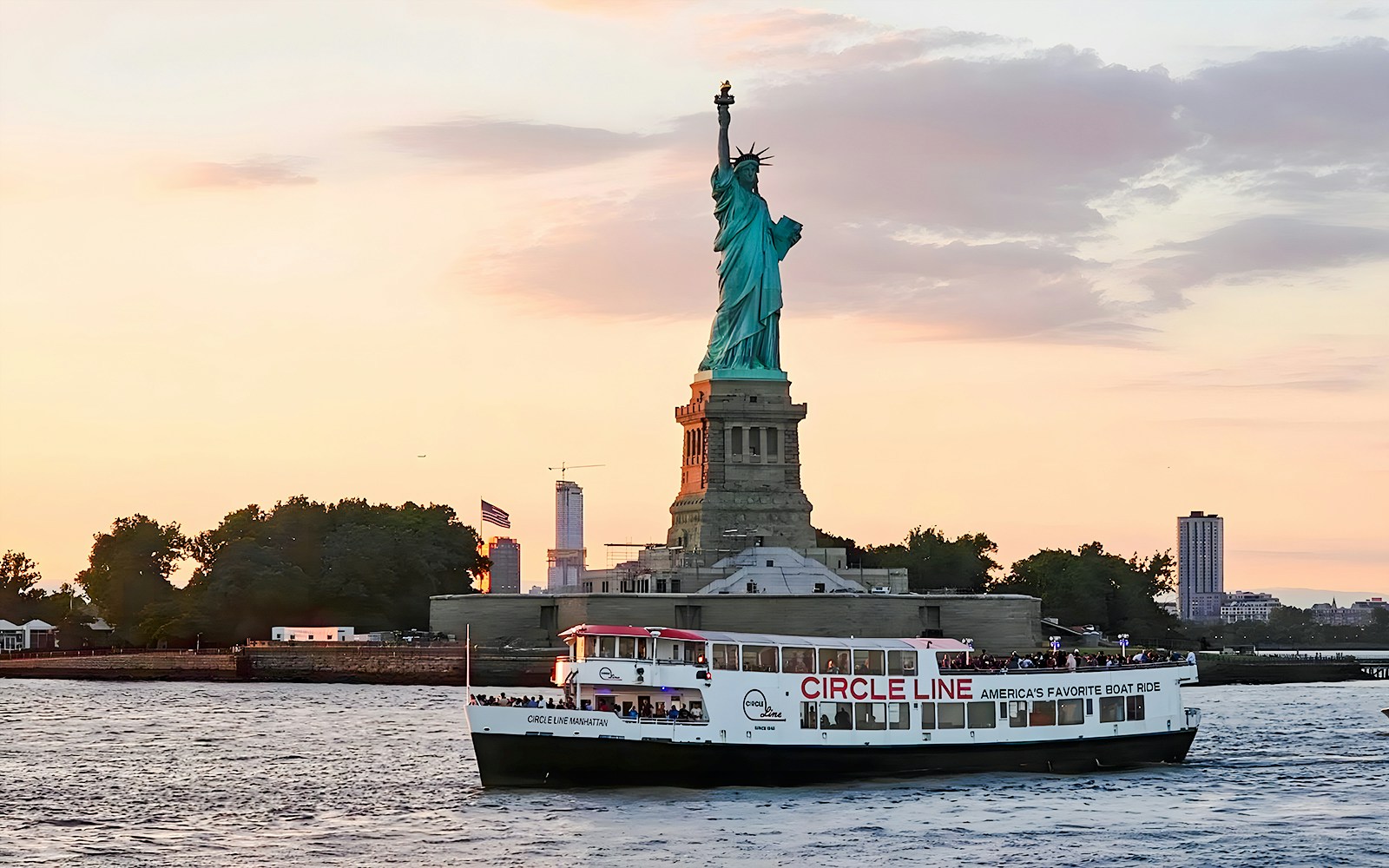 Statue of Liberty at sunset with Circle Line sightseeing cruise boat in New York Harbor.