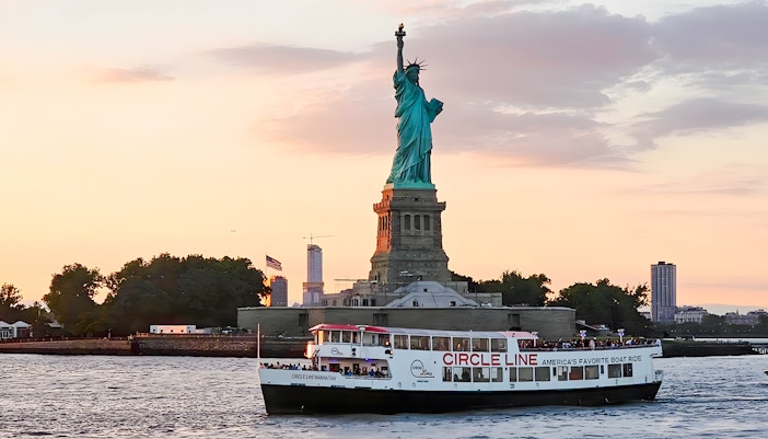 Statue of Liberty at sunset with Circle Line cruise boat in New York Harbor.
