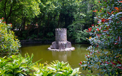 Stone tower surrounded by lush greenery in the gardens of Quinta da Regaleira, Sintra, Portugal.