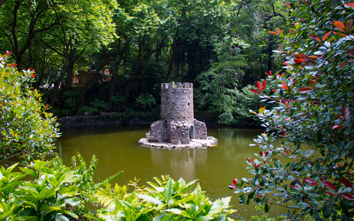 Stone tower surrounded by lush greenery in the gardens of Quinta da Regaleira, Sintra, Portugal.