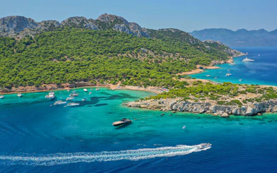 Boats sailing near lush green coastline of Agistri, Greece on a sunny day.