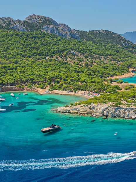 Boats sailing near lush green coastline of Agistri, Greece on a sunny day.