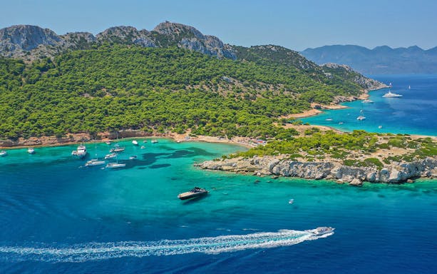 Boats sailing near lush green coastline of Agistri, Greece on a sunny day.