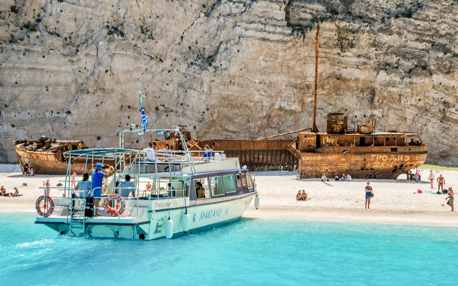 Glass bottom boat near shipwreck on Navagio Beach, Zakynthos, with tourists exploring the shore.