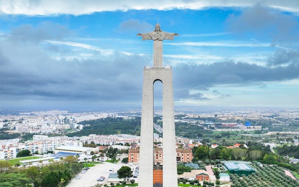 Christ the King statue overlooking Lisbon, Portugal, with cityscape in the background.