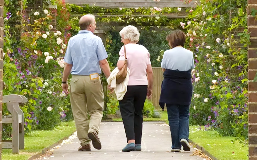 Visitors walking through a flower-covered archway at Kew Gardens.