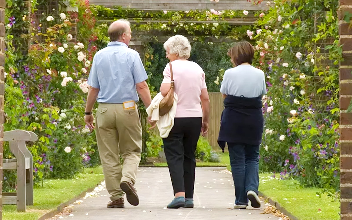Visitors walking through a flower-covered archway at Kew Gardens.