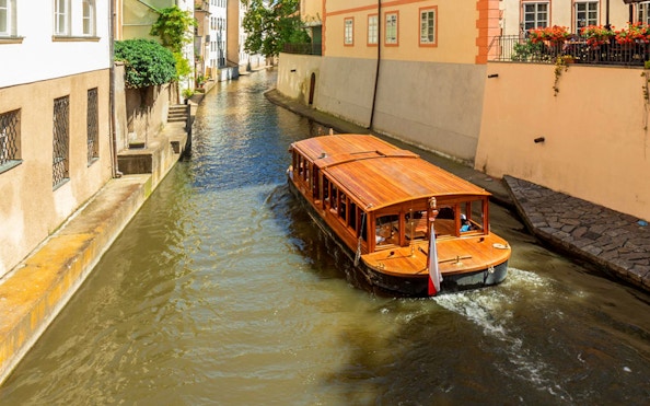 Wooden boat cruising a narrow canal in Prague, Czech Republic.