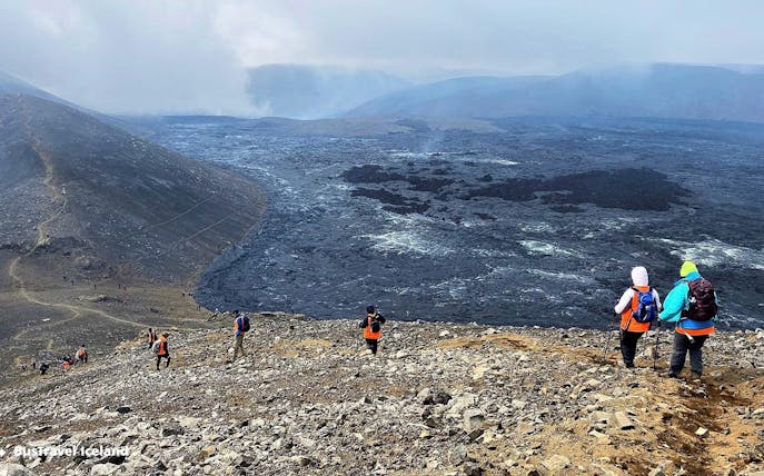 Hikers exploring volcanic terrain in Reykjanes, Iceland, with visible lava fields.