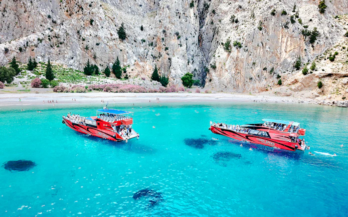 Boats in turquoise waters at St George's Bay, Rhodes, with swimmers nearby.