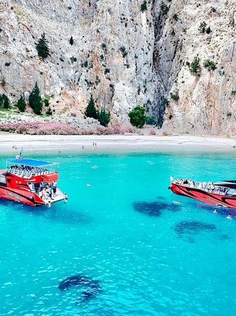 Boats in turquoise waters at St George's Bay, Rhodes, with swimmers nearby.