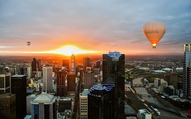 Hot air balloon over Melbourne skyline at sunrise.