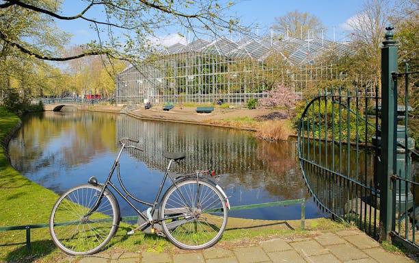 Bicycle by canal with reflections of Hortus Botanicus glasshouses, Amsterdam.