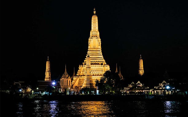 Wat Arun illuminated at night viewed from the Chao Phraya River, Bangkok.