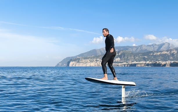 Person e-foiling on the sea near Capri with cliffs in the background.