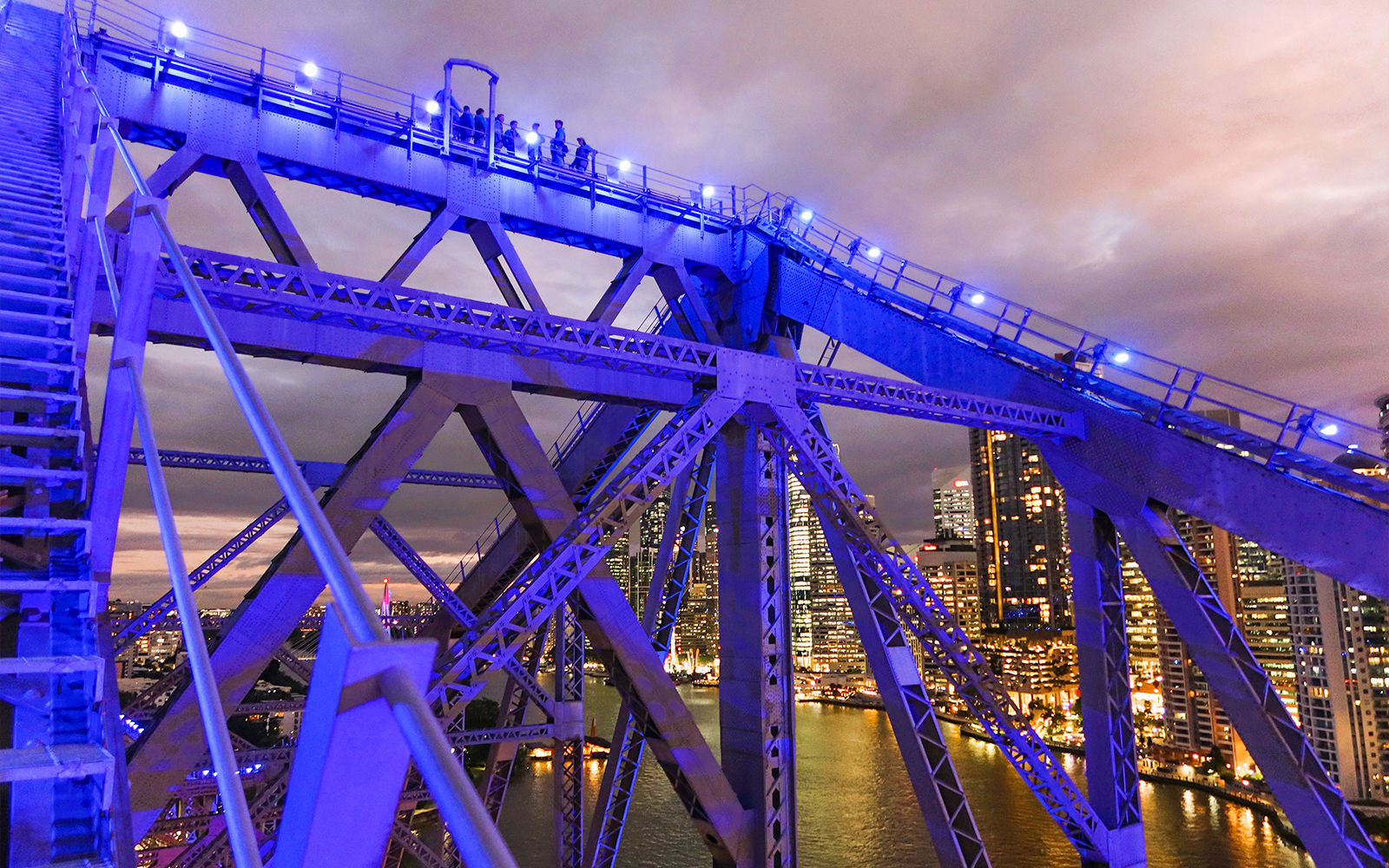 Climbers on Story Bridge at night with city skyline in Brisbane.
