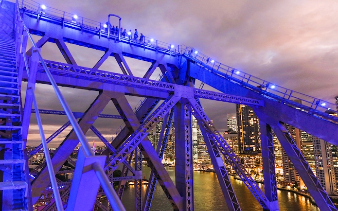 Climbers on Story Bridge at night with city skyline in Brisbane.