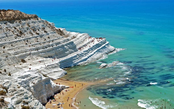 Scala dei Turchi limestone cliffs with visitors and turquoise sea in Sicily.