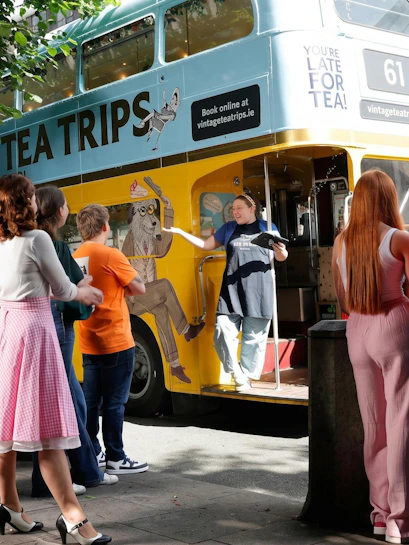 Afternoon tea bus tour in Dublin with guide welcoming passengers aboard vintage double-decker.