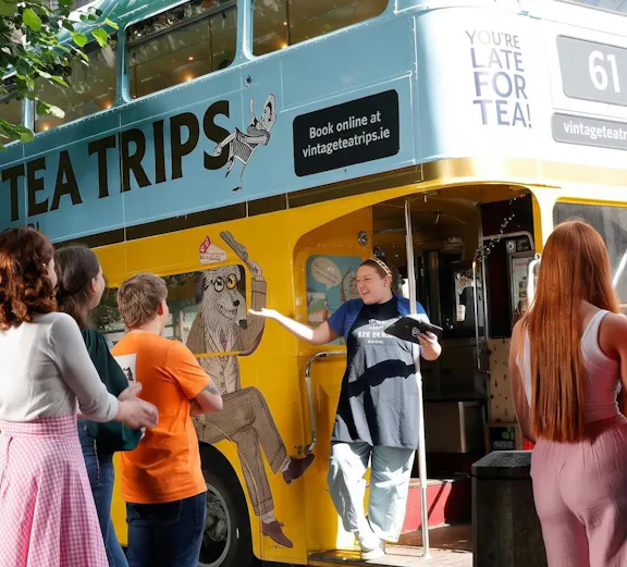 Afternoon tea bus tour in Dublin with guide welcoming passengers aboard vintage double-decker.