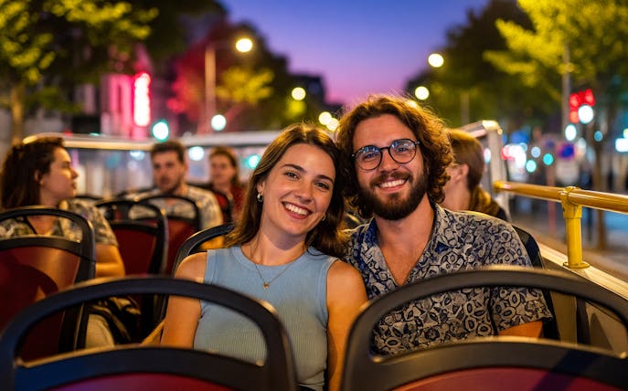 Tourists enjoying a city tour on a hop-on hop-off bus at dusk.