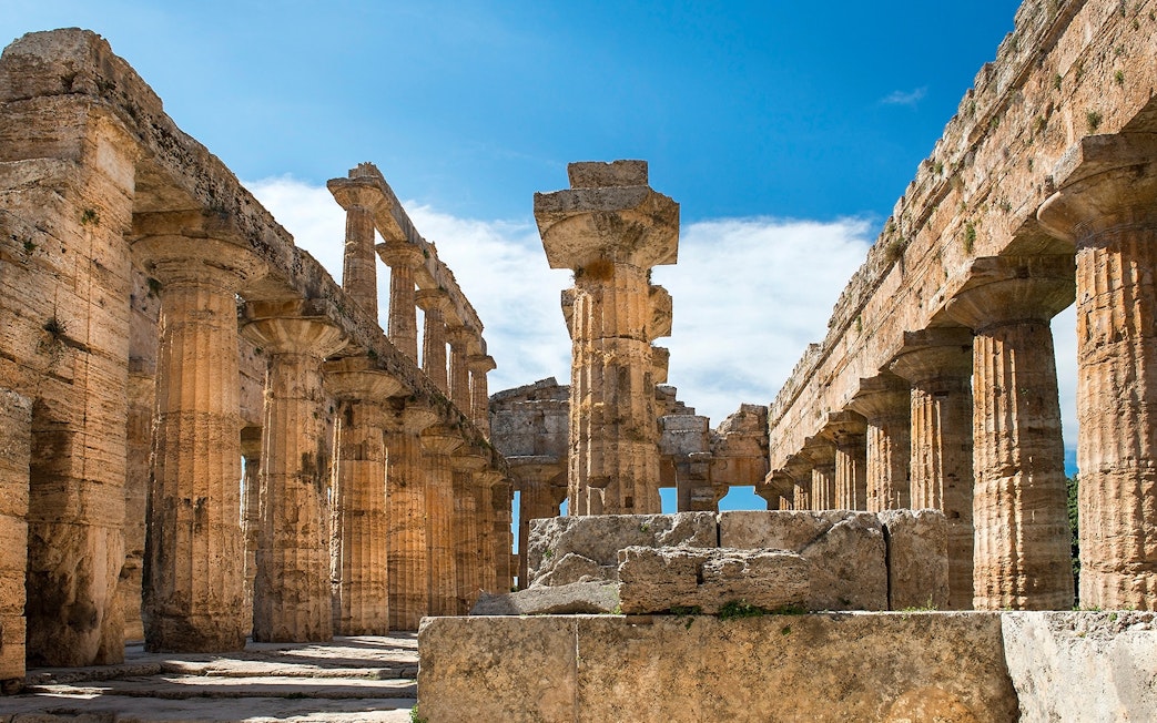 Ancient Greek temple ruins at Paestum, Italy, with stone columns and blue sky.