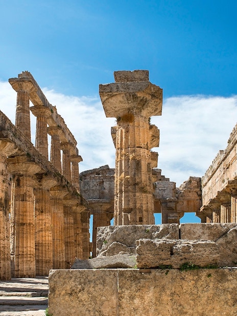 Ancient Greek temple ruins at Paestum, Italy, with stone columns and blue sky.