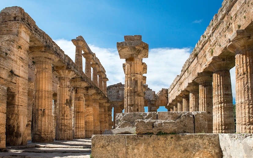 Ancient Greek temple ruins at Paestum, Italy, with stone columns and blue sky.