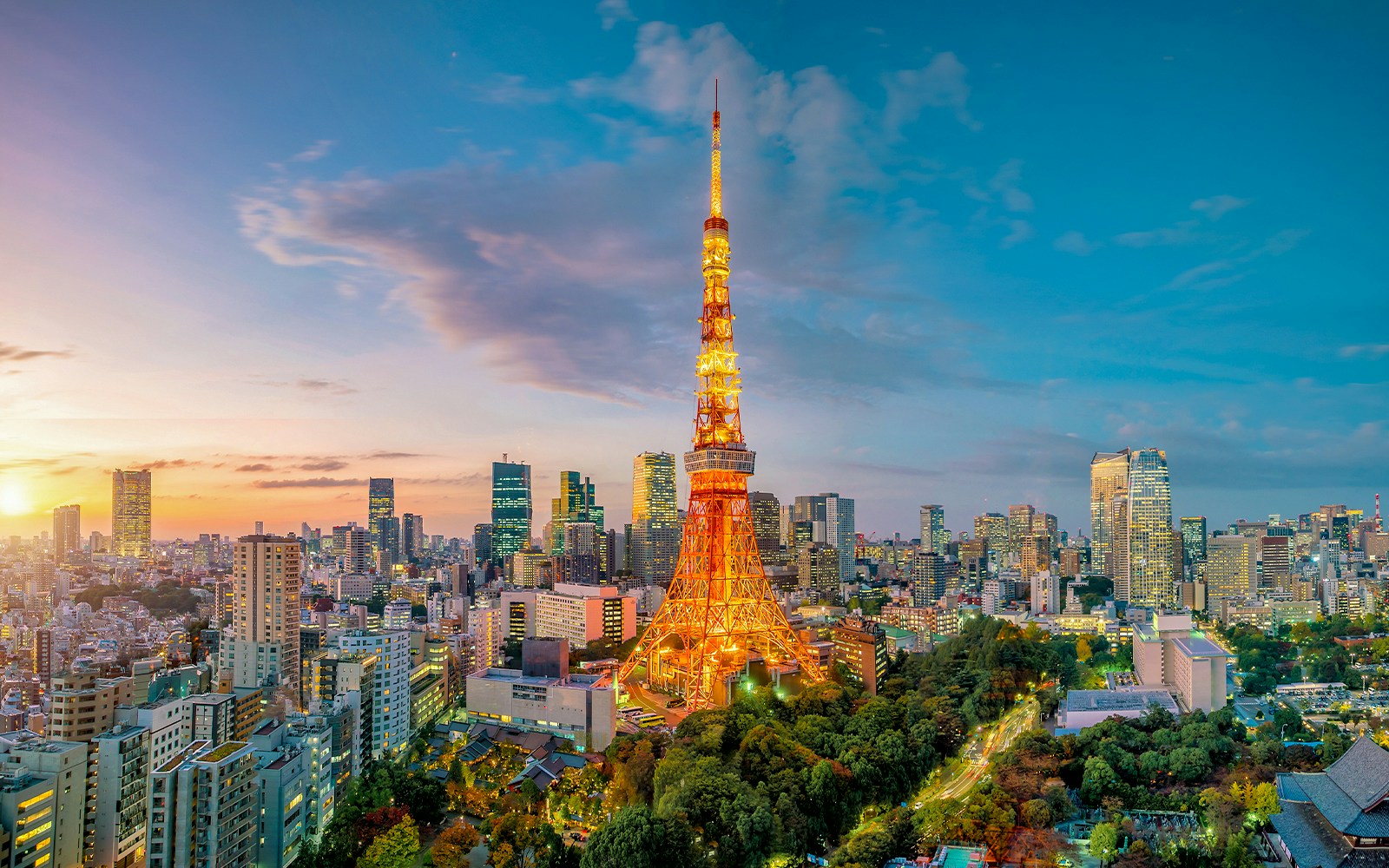 Die Tokyo Tower bei Dämmerung, beleuchtet, umgeben von modernen Hochhäusern und grünen Parks