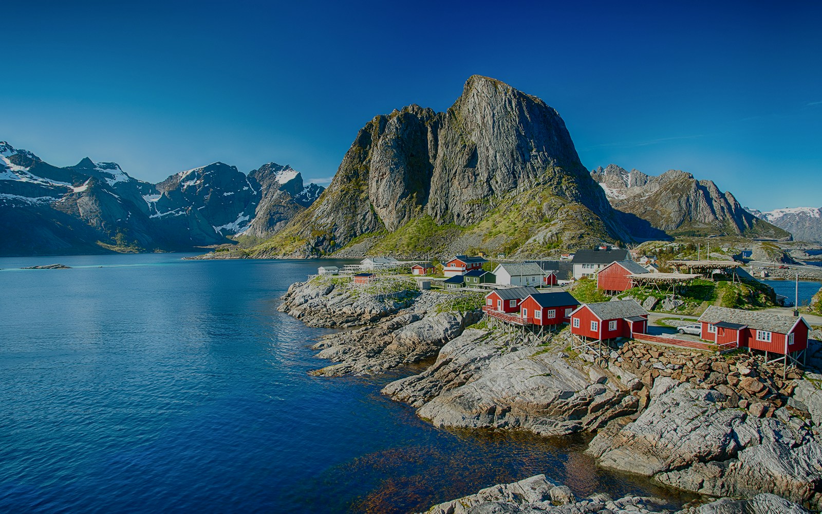 Red cabins on rocky shore with mountain backdrop in Lofoten, Norway.