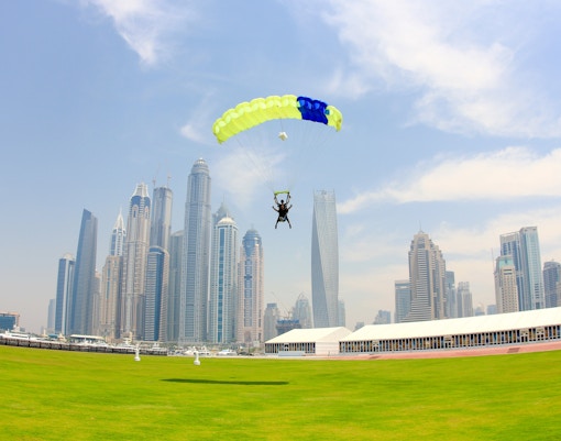 Skydiver landing on grass with Dubai skyline in the background.