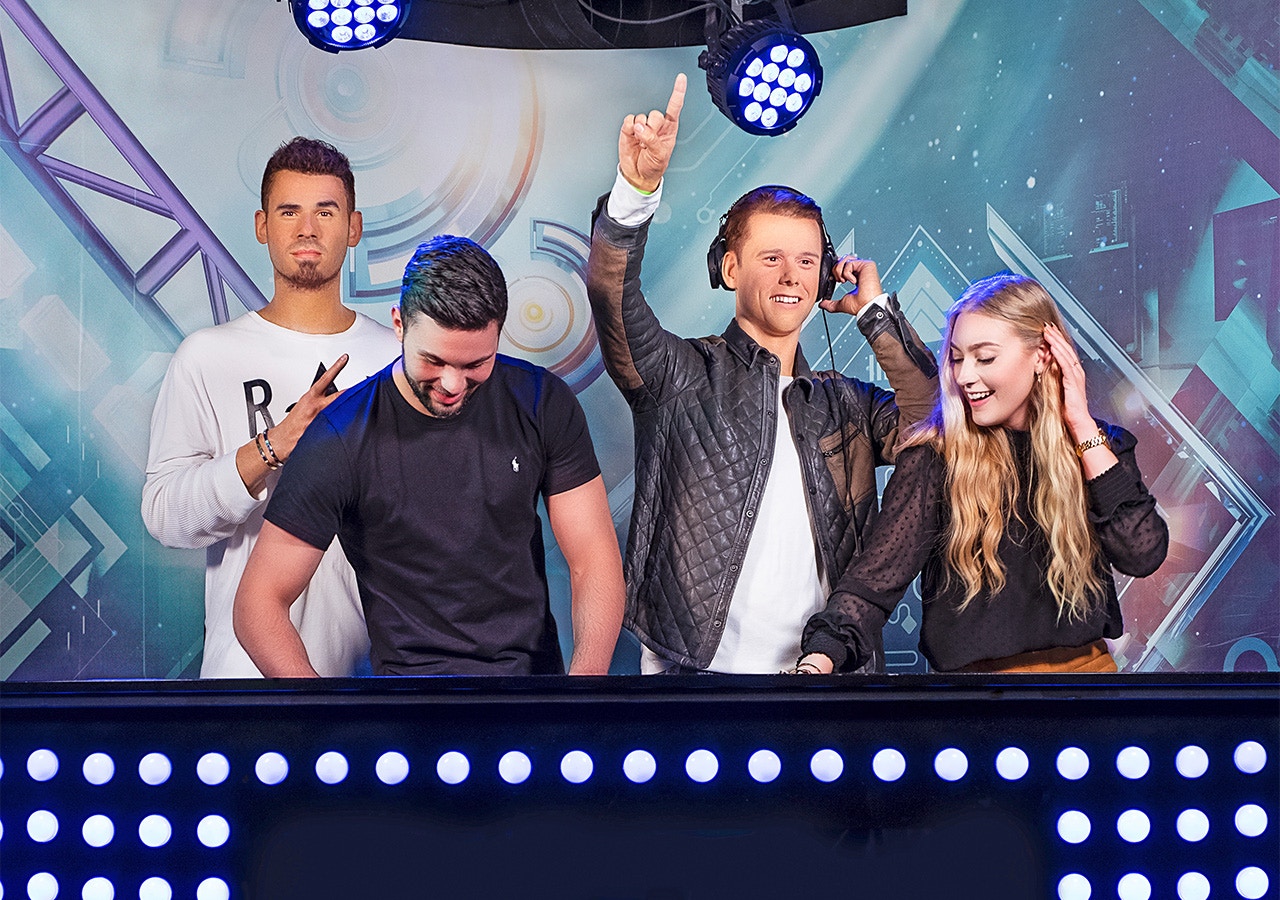 DJ figures at Madame Tussauds Amsterdam with vibrant lights and music-themed backdrop.