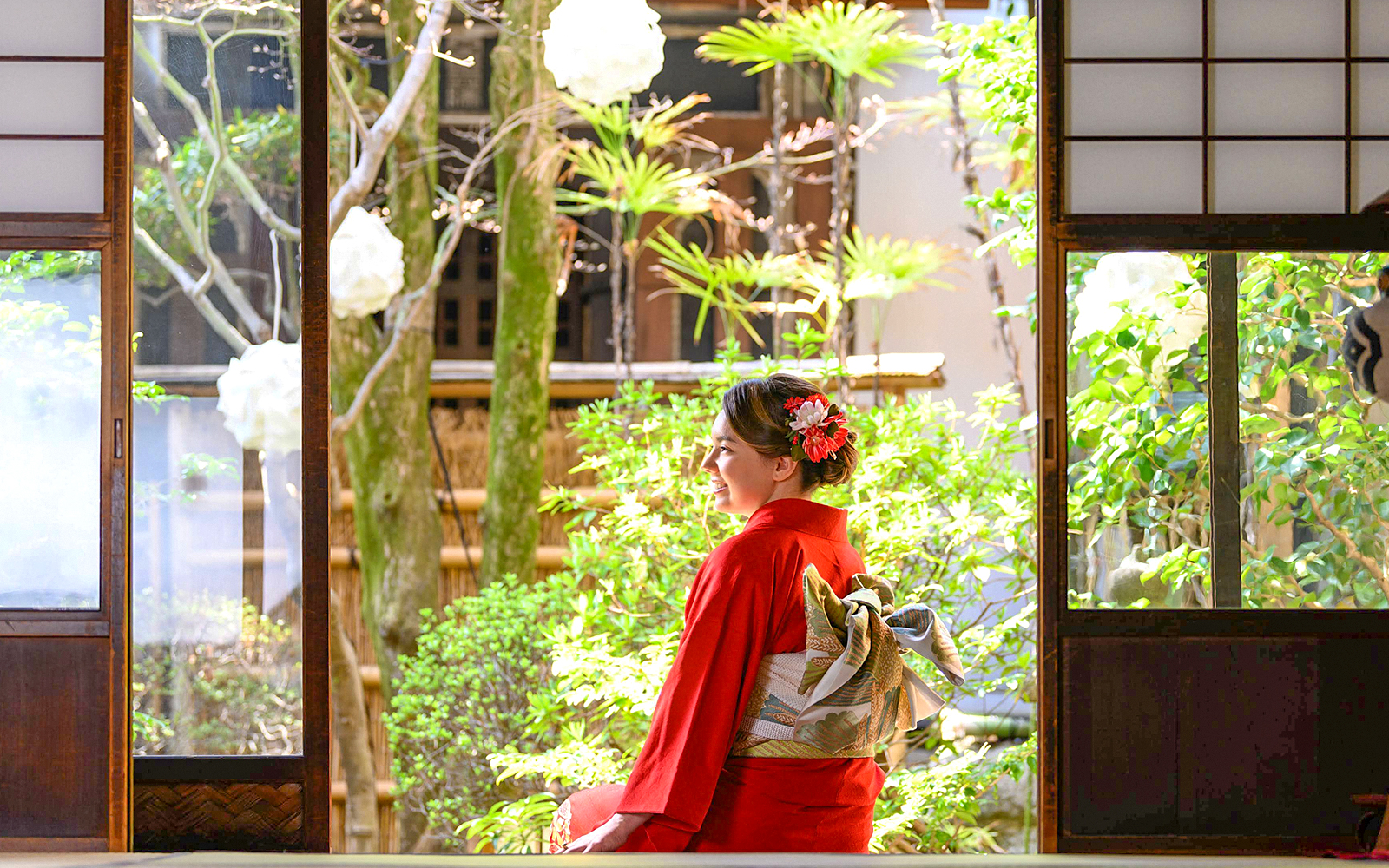 Tourist in red kimono sitting in traditional Japanese garden.