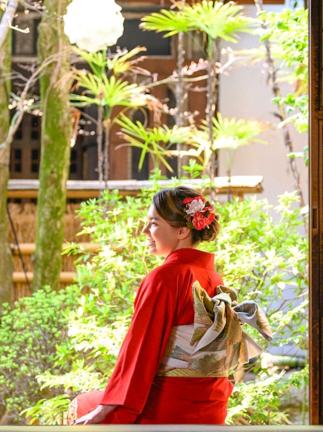 Tourist in red kimono sitting in traditional Japanese garden.
