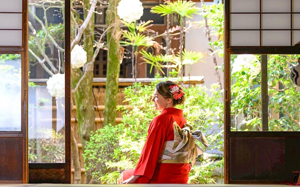 Tourist in red kimono sitting in traditional Japanese garden.