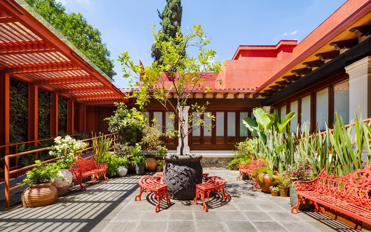 Courtyard of Museo Casa Kahlo with red benches and lush plants, Coyoacán, Mexico City.