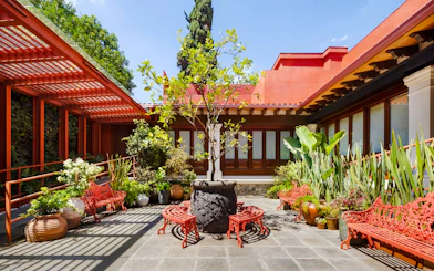 Courtyard of Museo Casa Kahlo with red benches and lush plants, Coyoacán, Mexico City.