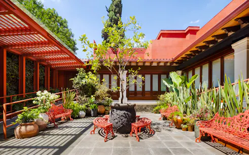 Courtyard of Museo Casa Kahlo with red benches and lush plants, Coyoacán, Mexico City.