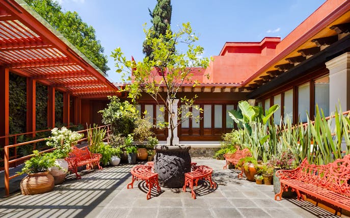 Courtyard of Museo Casa Kahlo with red benches and lush plants, Coyoacán, Mexico City.