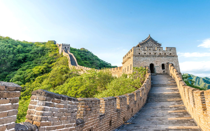 Great Wall of China winding through lush green hills under a clear blue sky.